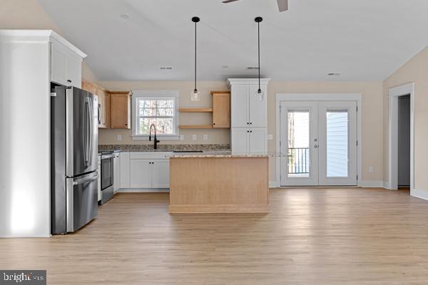 kitchen with stainless steel refrigerator, hanging light fixtures, a kitchen island, stove, and white cabinets