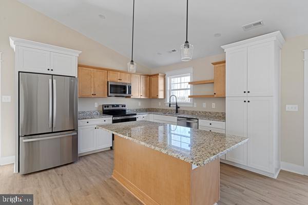 kitchen featuring light wood-type flooring, stainless steel appliances, pendant lighting, white cabinets, and a center island