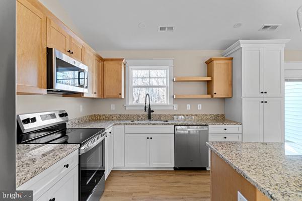 kitchen with sink, stainless steel appliances, light stone counters, white cabinets, and light wood-type flooring