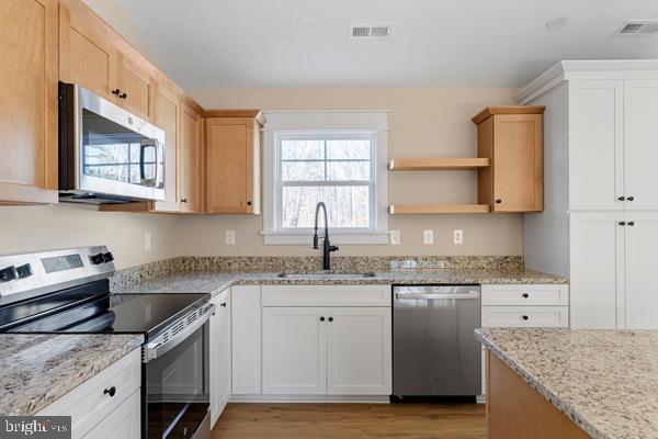 kitchen with white cabinets, sink, light hardwood / wood-style flooring, light stone counters, and stainless steel appliances