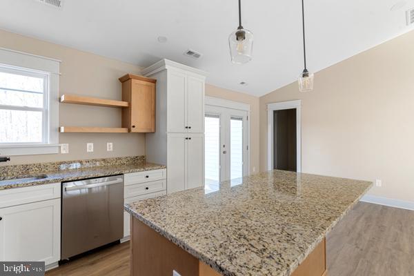 kitchen featuring stainless steel dishwasher, decorative light fixtures, a kitchen island, light stone counters, and white cabinetry