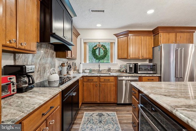 kitchen featuring dark hardwood / wood-style flooring, appliances with stainless steel finishes, a textured ceiling, light stone countertops, and sink