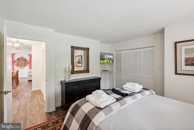 bedroom with a textured ceiling, wood-type flooring, and a closet