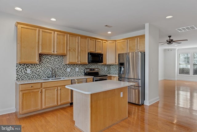 kitchen featuring appliances with stainless steel finishes, light wood-type flooring, backsplash, sink, and a kitchen island