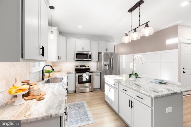 kitchen with white cabinets, sink, light hardwood / wood-style floors, appliances with stainless steel finishes, and a kitchen island