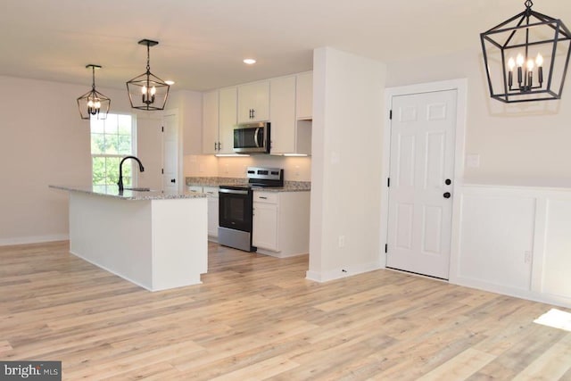 kitchen with white cabinetry, appliances with stainless steel finishes, a center island with sink, and hanging light fixtures