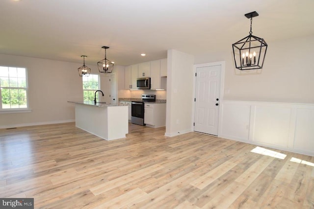 kitchen featuring hanging light fixtures, an island with sink, white cabinetry, light wood-type flooring, and stainless steel appliances