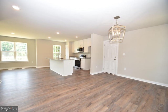 kitchen with an island with sink, dark hardwood / wood-style flooring, hanging light fixtures, white cabinetry, and stainless steel appliances