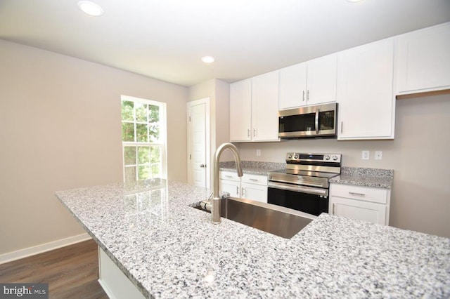 kitchen with dark wood-type flooring, appliances with stainless steel finishes, light stone counters, and white cabinetry