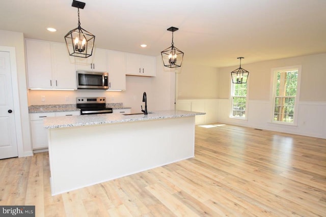 kitchen with light hardwood / wood-style floors, stainless steel appliances, a center island with sink, and white cabinets