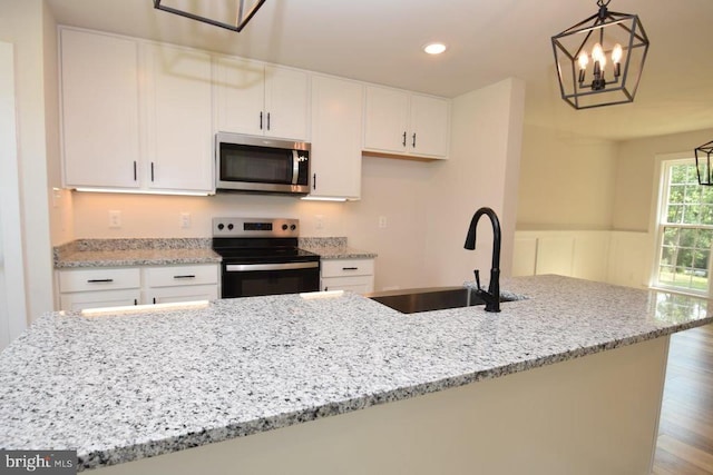 kitchen with sink, stainless steel appliances, decorative light fixtures, white cabinets, and hardwood / wood-style flooring