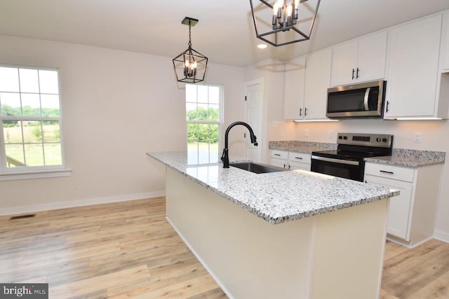 kitchen featuring sink, white cabinetry, stainless steel appliances, decorative light fixtures, and a kitchen island with sink