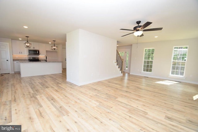 unfurnished living room featuring sink, ceiling fan with notable chandelier, and light wood-type flooring