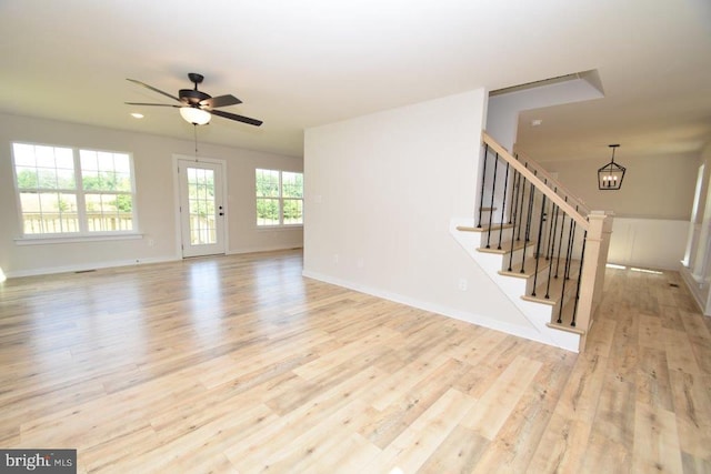 unfurnished living room with light wood-type flooring and ceiling fan with notable chandelier