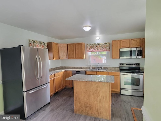 kitchen with light stone counters, stainless steel appliances, sink, light hardwood / wood-style floors, and a center island