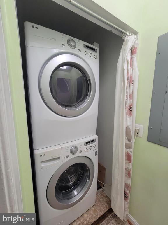 clothes washing area with electric panel and stacked washer and clothes dryer