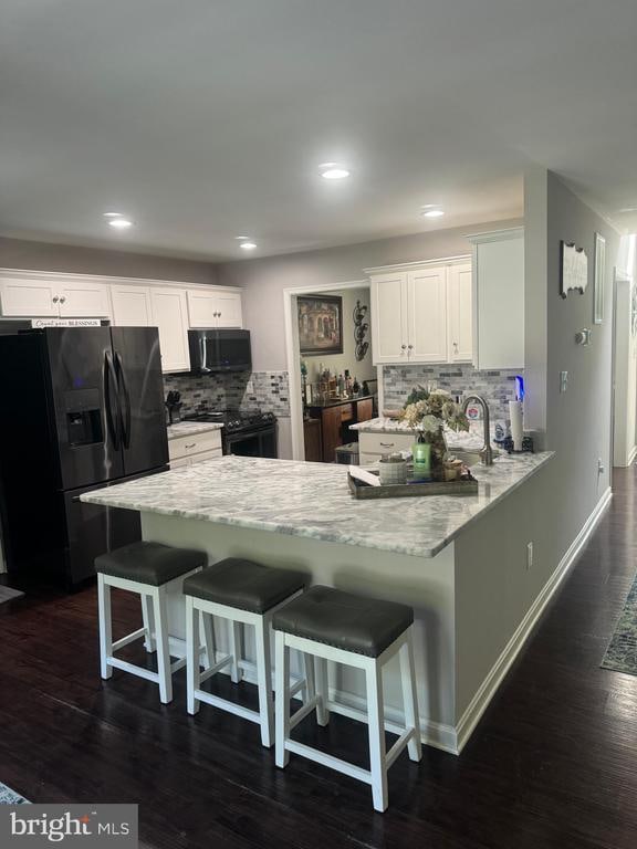 kitchen with black appliances, a breakfast bar area, white cabinets, dark wood-type flooring, and decorative backsplash