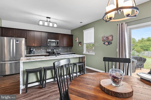 kitchen with pendant lighting, appliances with stainless steel finishes, a center island with sink, and dark brown cabinets