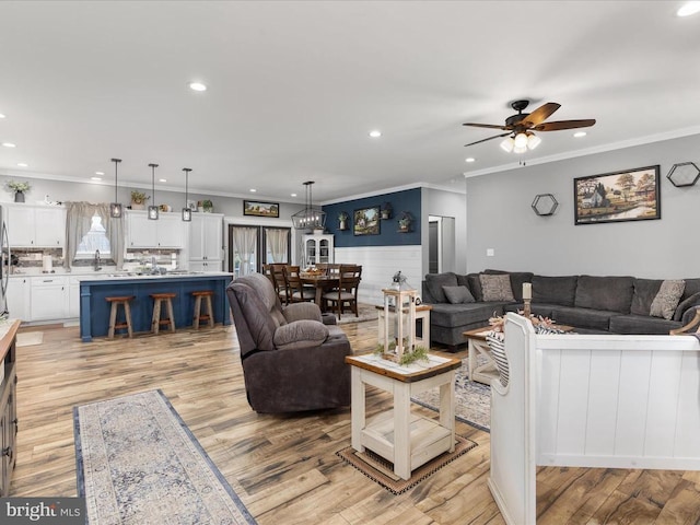 living room with ceiling fan with notable chandelier, light wood-type flooring, and crown molding