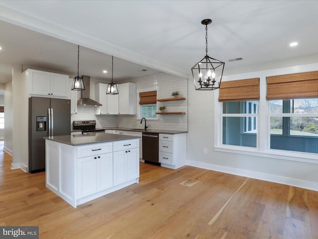 kitchen featuring white cabinets, stainless steel appliances, wall chimney exhaust hood, and decorative light fixtures