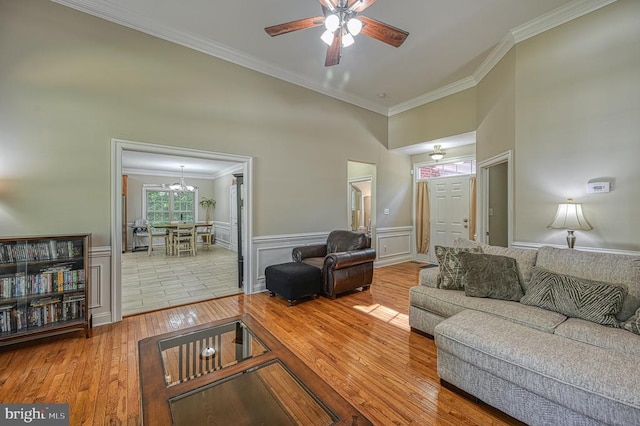 living room featuring wood-type flooring, ceiling fan with notable chandelier, ornamental molding, and a high ceiling