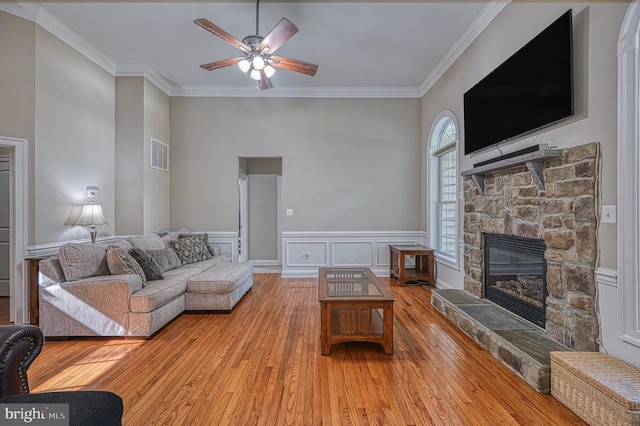 living room featuring ornamental molding, a high ceiling, ceiling fan, hardwood / wood-style floors, and a stone fireplace