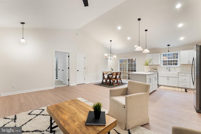 living room with high vaulted ceiling, an inviting chandelier, light wood-type flooring, and sink