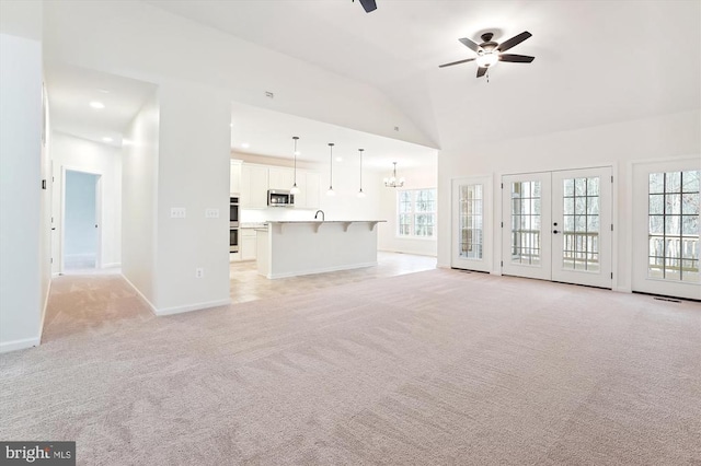 unfurnished living room with high vaulted ceiling, ceiling fan with notable chandelier, light carpet, and plenty of natural light