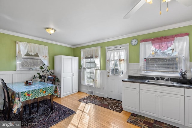 kitchen featuring ceiling fan, sink, crown molding, white cabinets, and light wood-type flooring