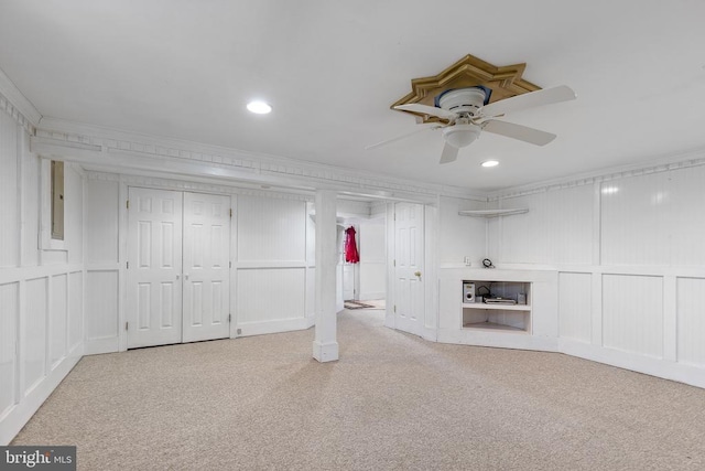 basement with light carpet, electric panel, ceiling fan, and ornamental molding