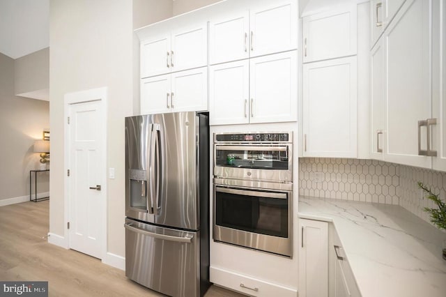 kitchen featuring light hardwood / wood-style flooring, appliances with stainless steel finishes, tasteful backsplash, light stone counters, and white cabinetry