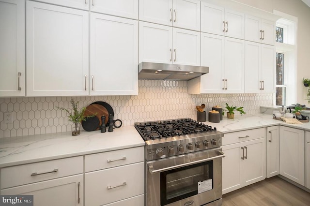 kitchen with light stone counters, light hardwood / wood-style flooring, high end stove, decorative backsplash, and white cabinets