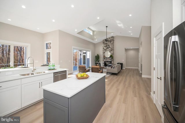 kitchen with white cabinets, sink, a fireplace, a kitchen island, and stainless steel appliances