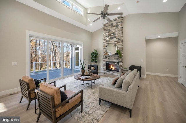 living room featuring a stone fireplace, a wealth of natural light, light hardwood / wood-style flooring, and high vaulted ceiling