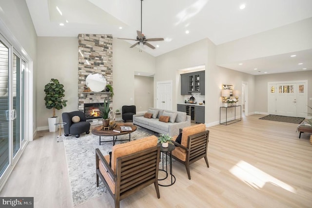 living room featuring ceiling fan, a fireplace, high vaulted ceiling, and light wood-type flooring