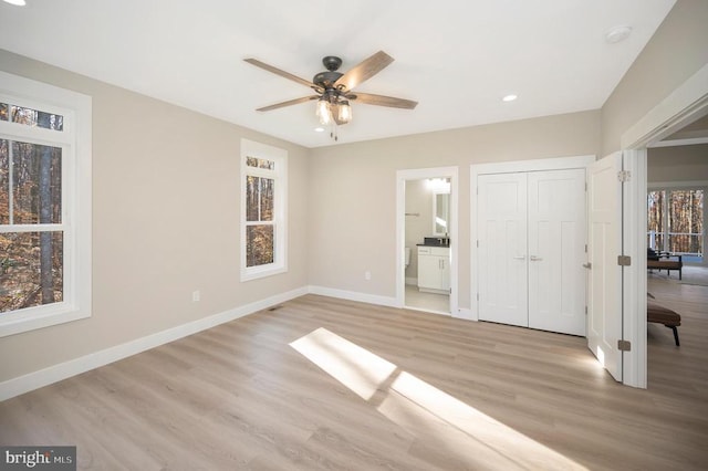 unfurnished bedroom featuring ceiling fan, light hardwood / wood-style floors, ensuite bath, and multiple windows