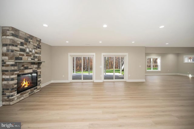 unfurnished living room with light wood-type flooring, a stone fireplace, and a healthy amount of sunlight