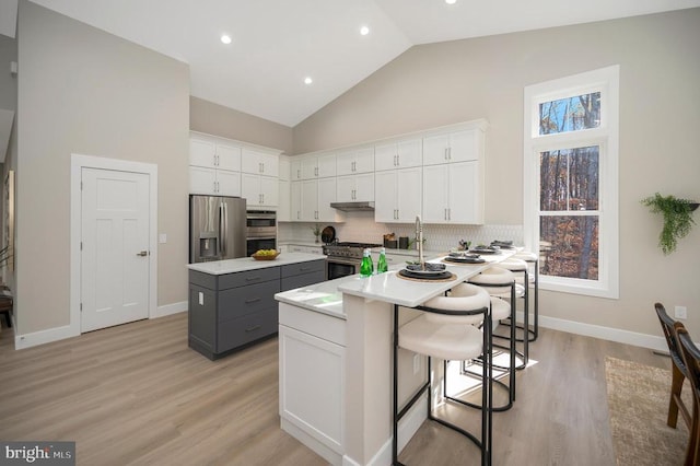 kitchen featuring a breakfast bar, gray cabinets, white cabinetry, and stainless steel appliances