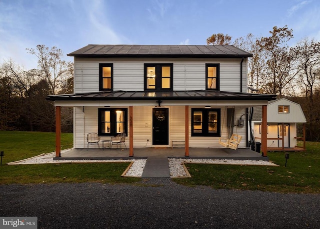 back house at dusk with a lawn and covered porch