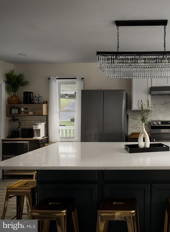 kitchen with a kitchen bar, light stone countertops, backsplash, stainless steel appliances, and pendant lighting