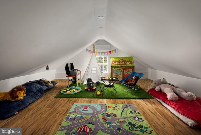 playroom with a wall unit AC, wood-type flooring, and vaulted ceiling