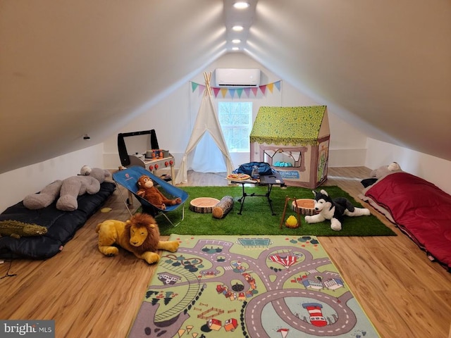 bedroom with a wall mounted AC, wood-type flooring, and vaulted ceiling