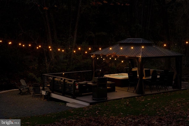 patio at twilight featuring a gazebo, a hot tub, and a deck