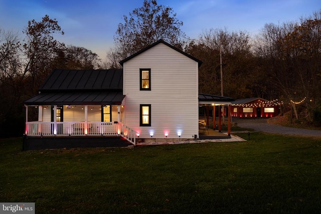 back house at dusk with a lawn and covered porch