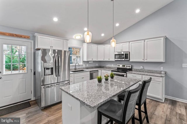 kitchen featuring lofted ceiling, white cabinets, hanging light fixtures, appliances with stainless steel finishes, and a kitchen island