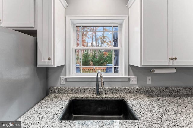 kitchen featuring white cabinets, light stone countertops, and sink