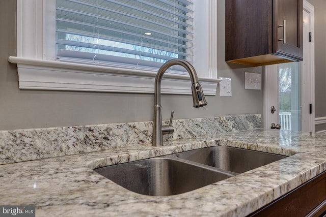 details with dark brown cabinetry, light stone counters, and sink