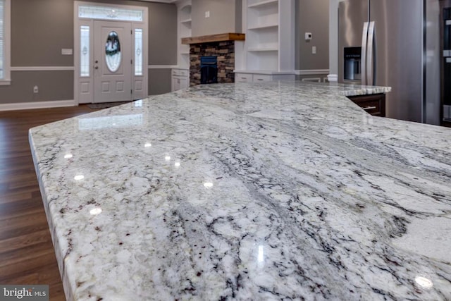 kitchen featuring dark hardwood / wood-style flooring, a stone fireplace, light stone counters, and built in shelves