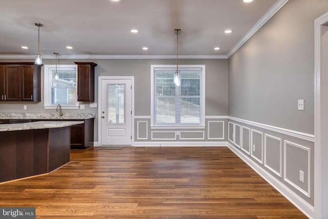 kitchen featuring light stone countertops, pendant lighting, hardwood / wood-style flooring, and crown molding