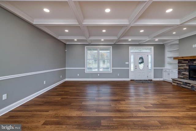 unfurnished living room featuring dark wood-type flooring, coffered ceiling, a stone fireplace, ornamental molding, and beamed ceiling